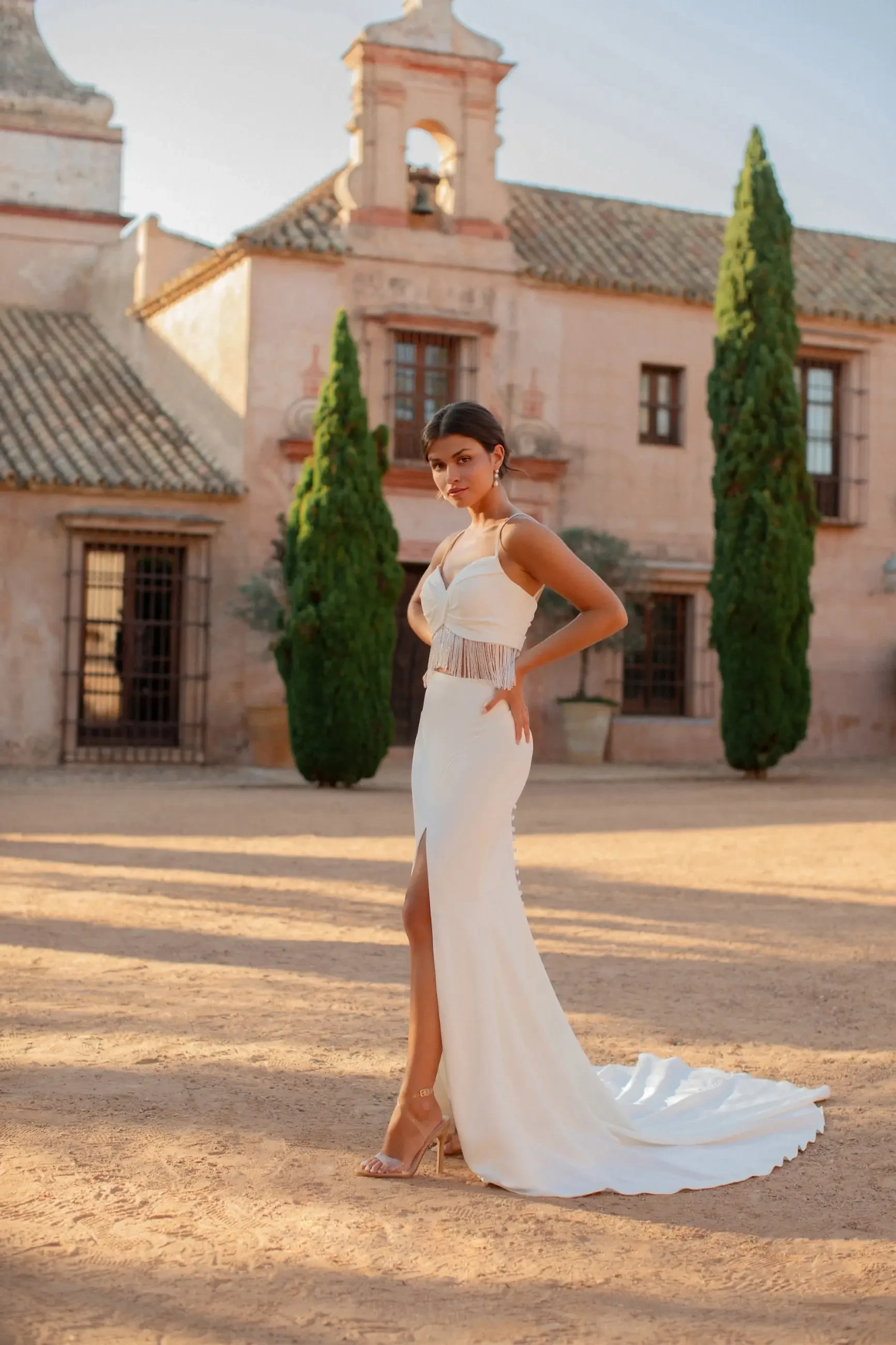 Model is wearing a sleeveless sheath wedding dress with a corset illusion bodice