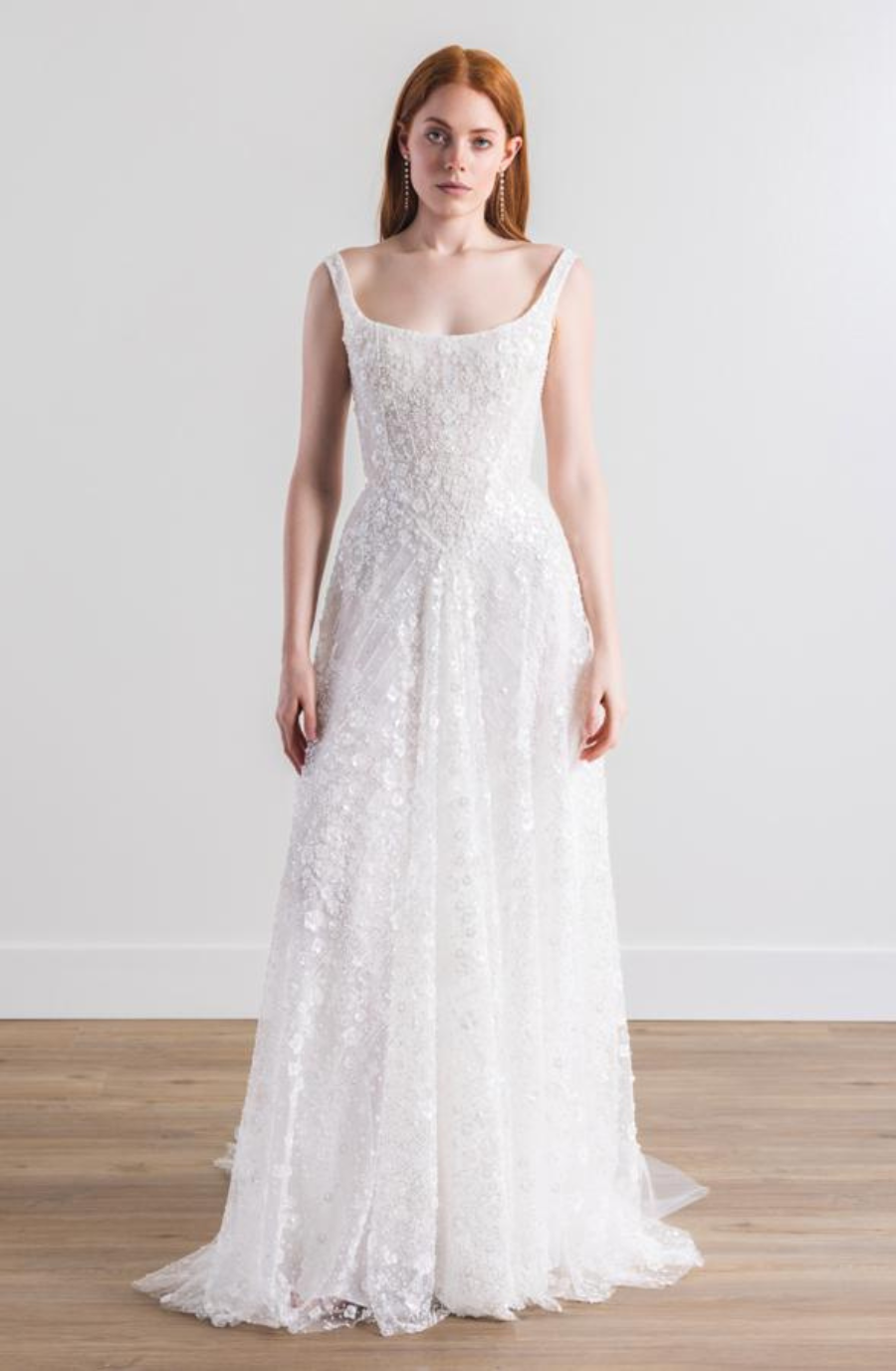 Model is wearing a sleeveless a-line bridal gown with a basque waist and lace fabric