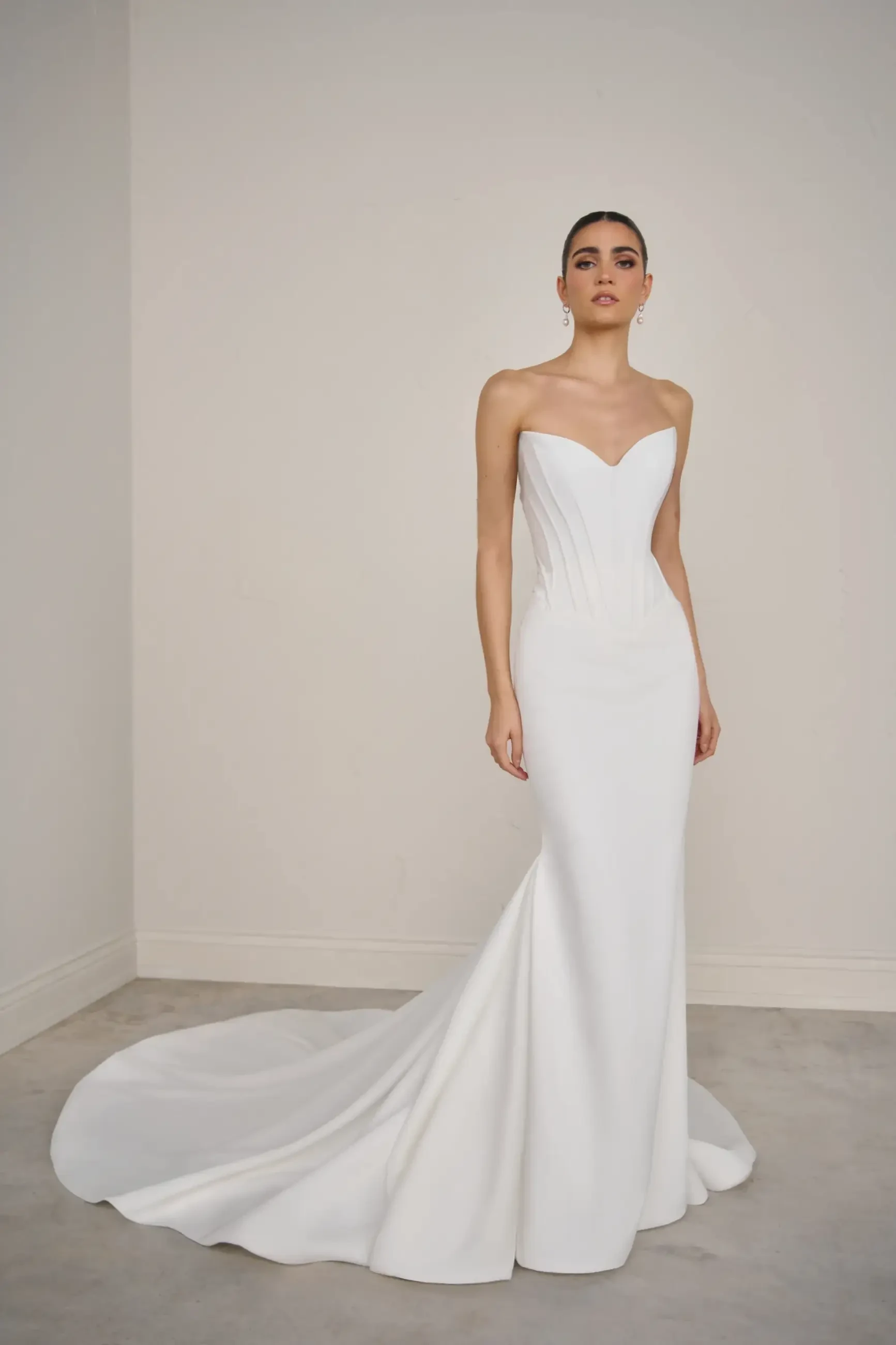 A model wearing a strapless white wedding dress with a fitted bodice and a long train, standing against a neutral background.
