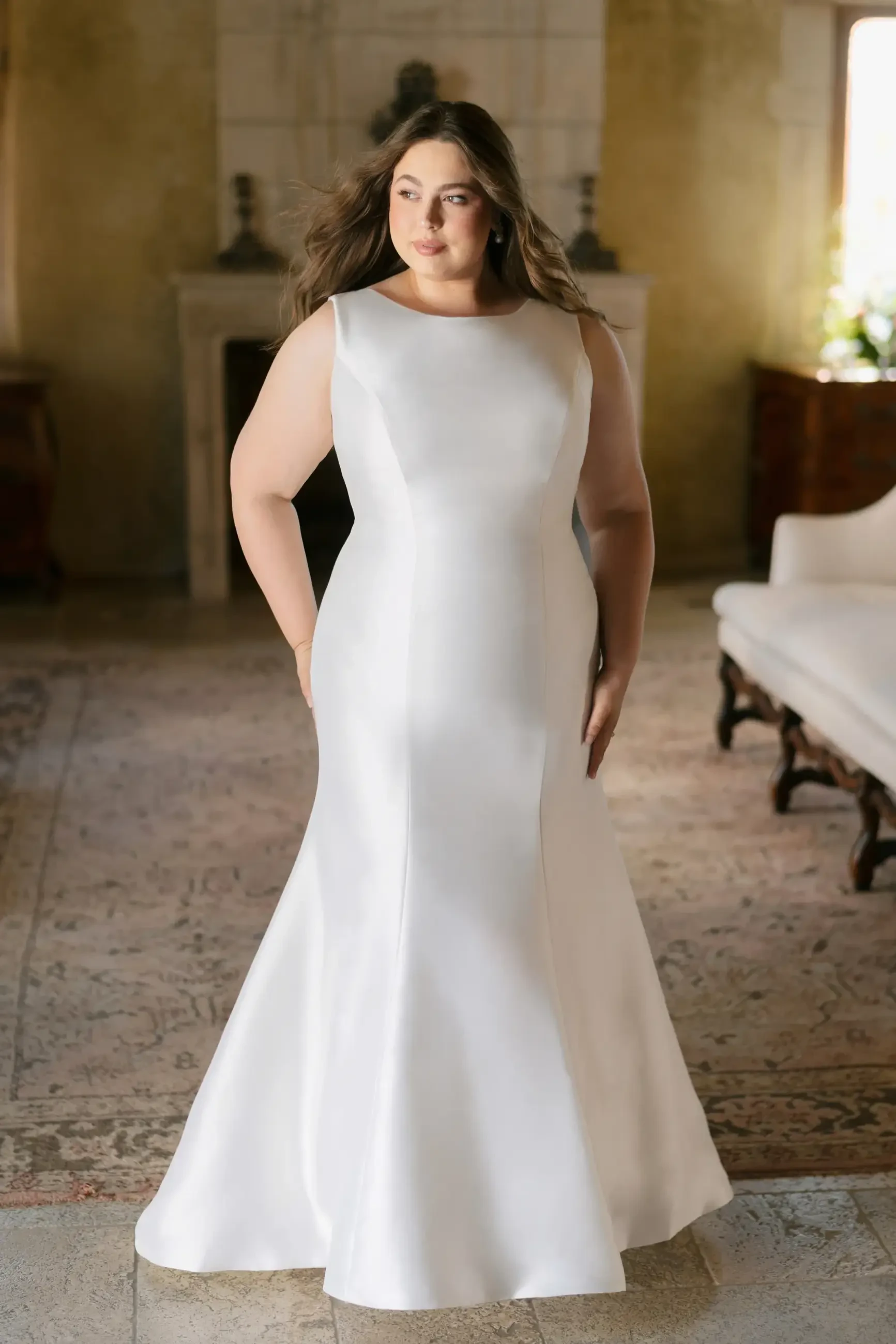 A person wearing a white wedding dress, standing in a well-lit room with a vintage decor.